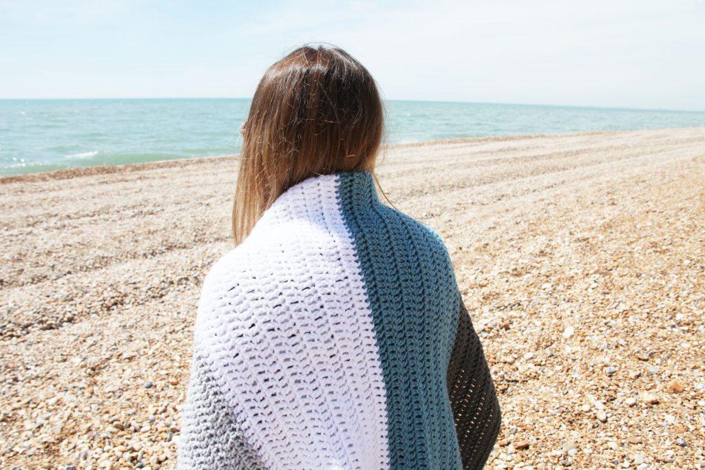Girl on a beach with a block stripe crochet blanket over her shoulders