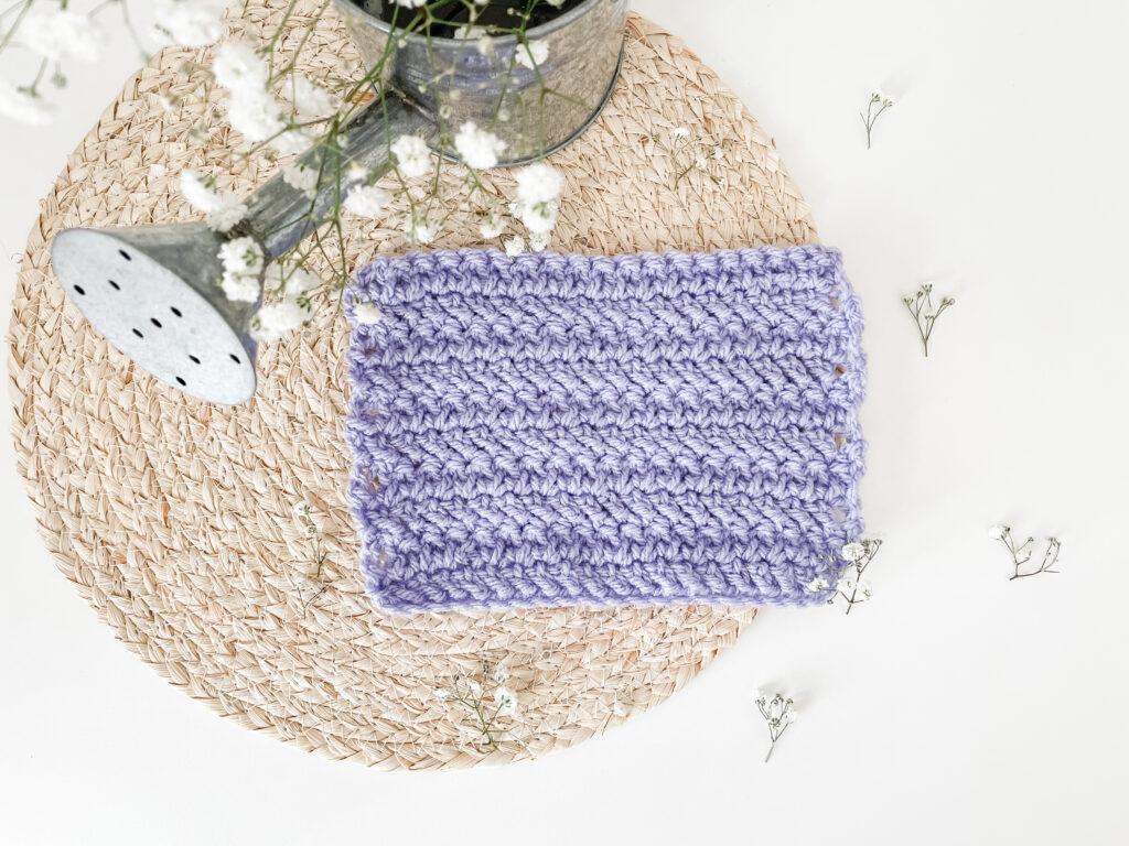 The herringbone treble stitch in purple yarn with a watering can