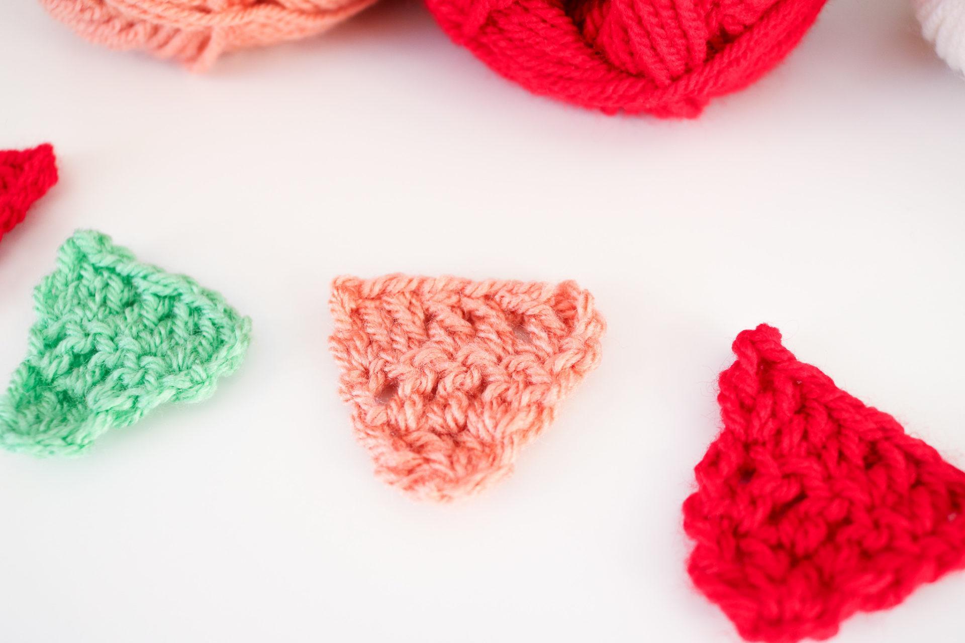 flay lay image of three mini crochet triangles made in green, coral and red yarn. 