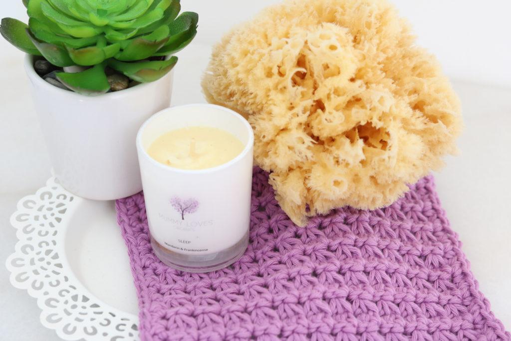 A purple crochet wash cloth with a candle and plant.