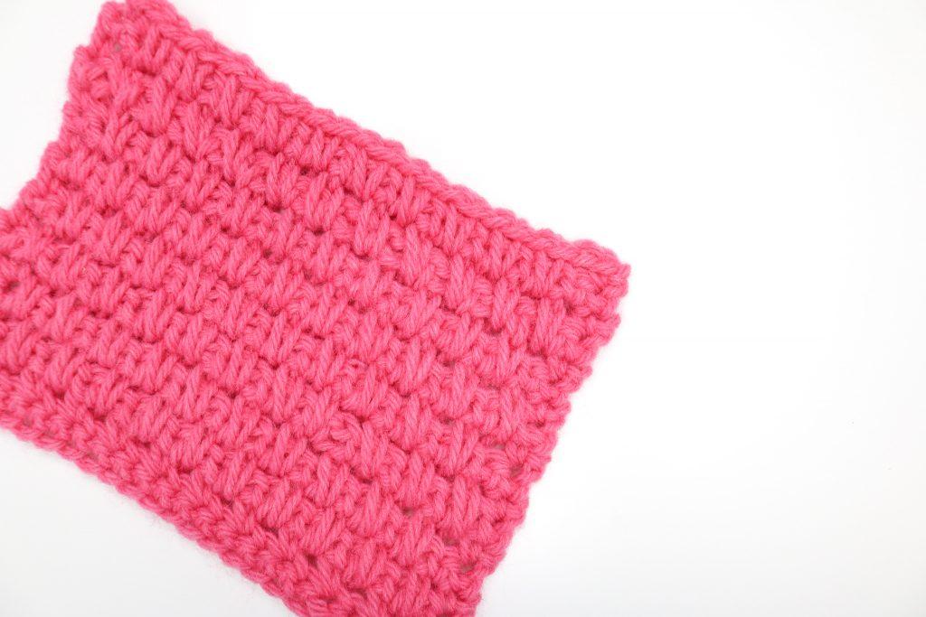 Moss stitch swatch in pink yarn on a white background.