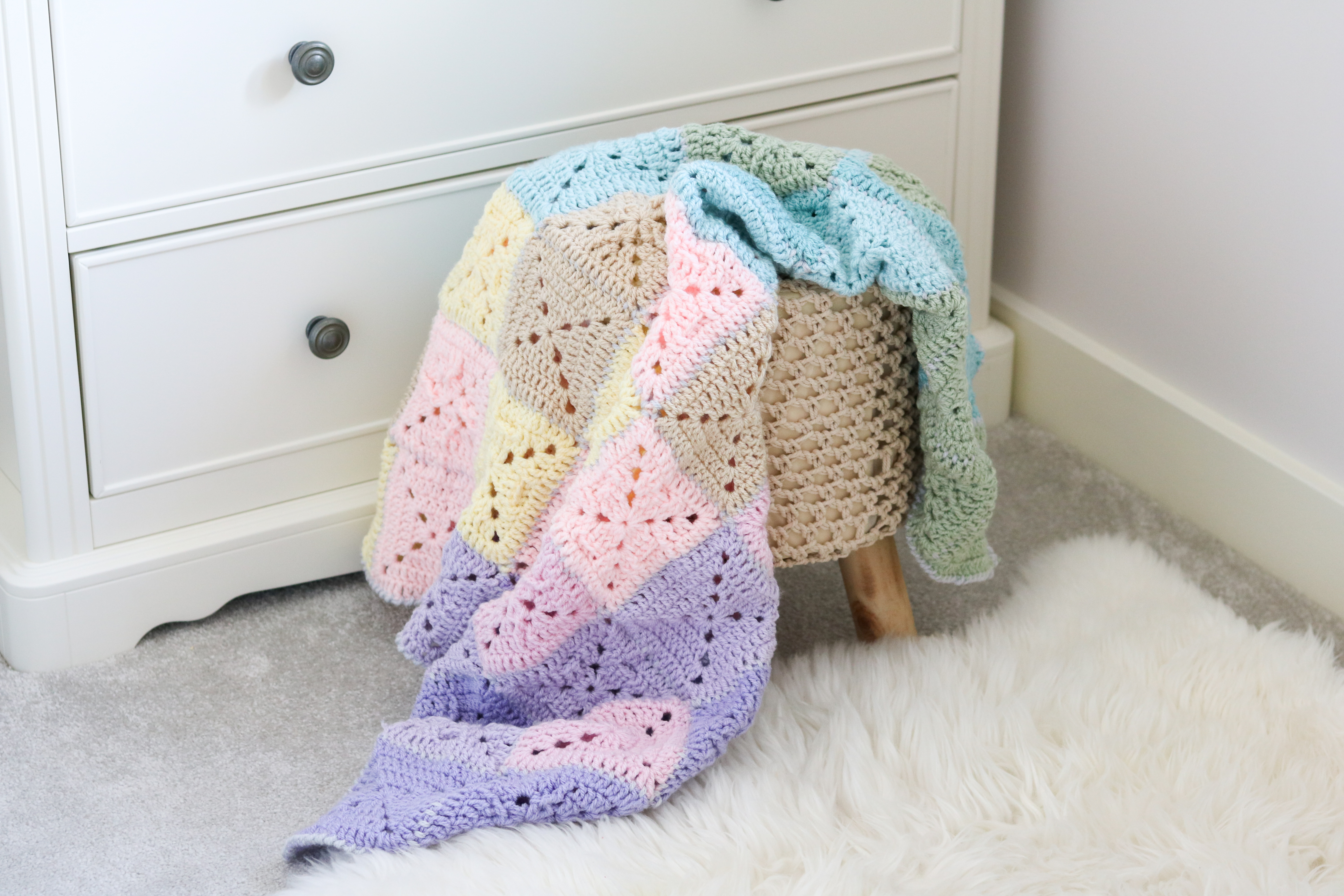 pastel crochet blanket draped over a stool