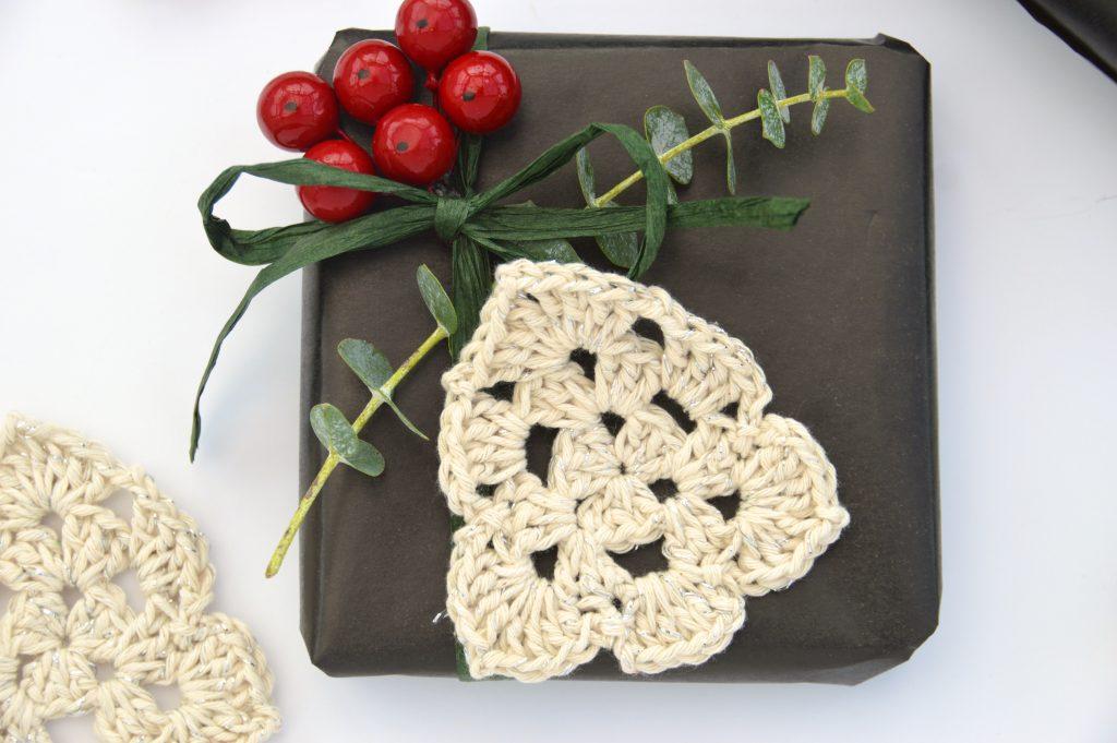 Crochet Christmas Tree made in cream yarn lay flat on a wrapped present with foliage and berries. 