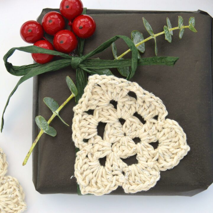 flat lay image of Crochet Christmas Tree made in cream yarn attached to a wrapped present with foliage and berries.