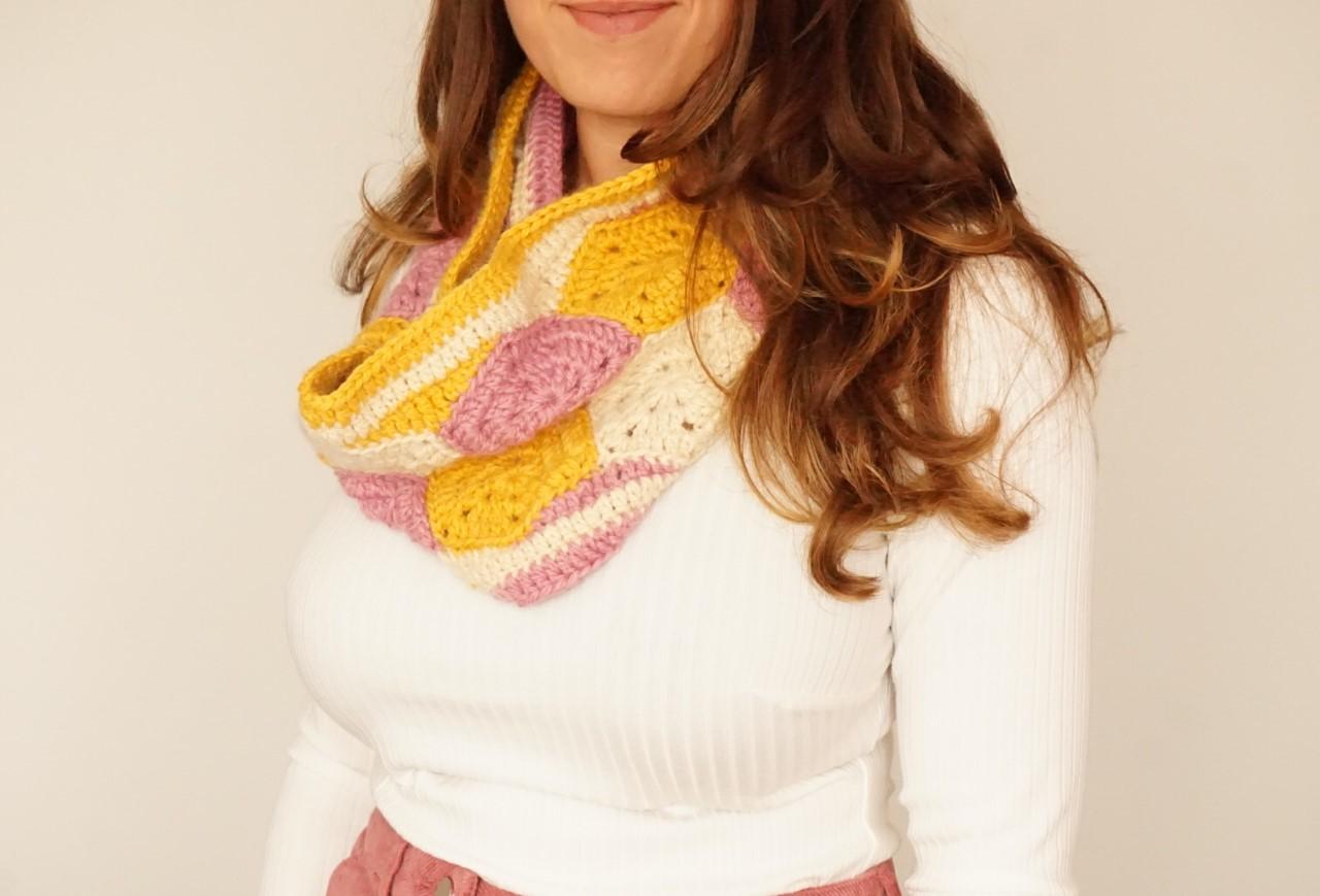 a women wearing a yellow,cream and pink crochet hexagon cowl stood in front of cream backdrop