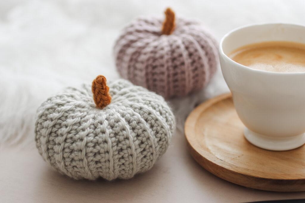 Two crochet pumpkins sat alongside a cup of coffee on a wooden coaster. 