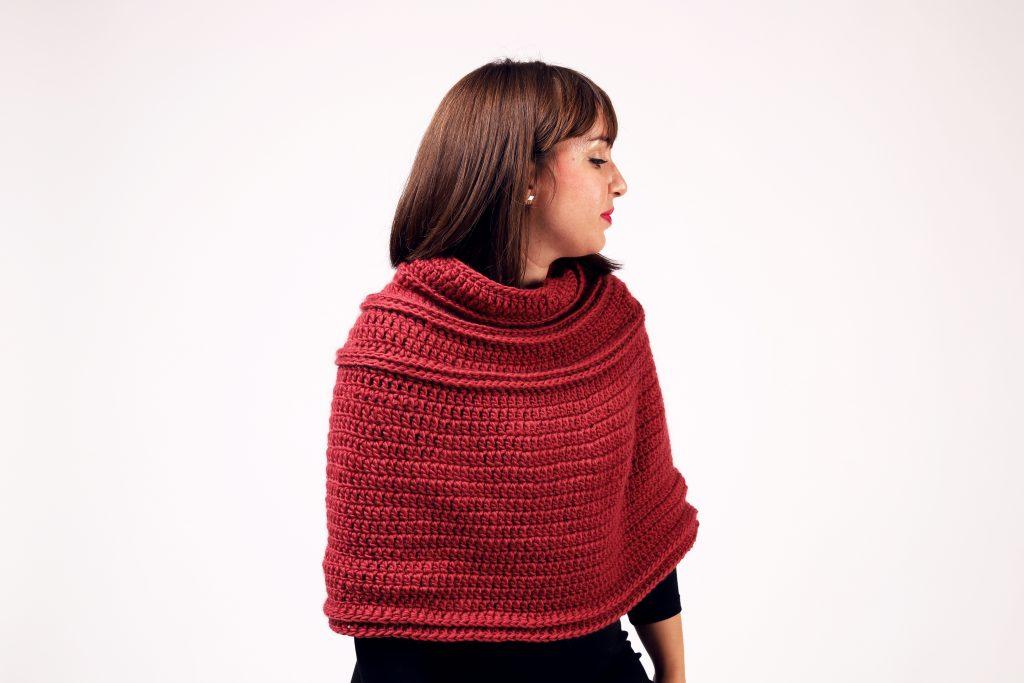 A woman is wearing a rich red crochet cape. She is looking to the right of the screen.