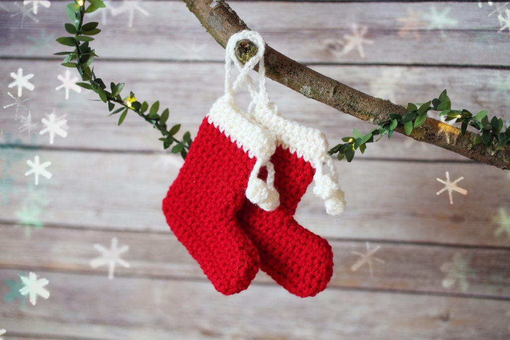 A pair of crochet christmas stockings are hung on a natural branch.