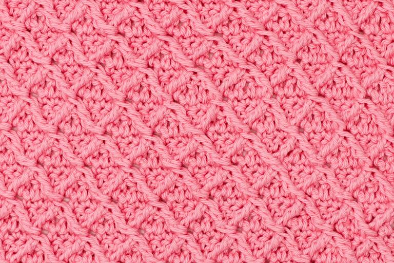 Close-up of pink crochet fabric featuring the diamond waffle stitch pattern, showing textured diagonal ridges and raised diamond shapes.