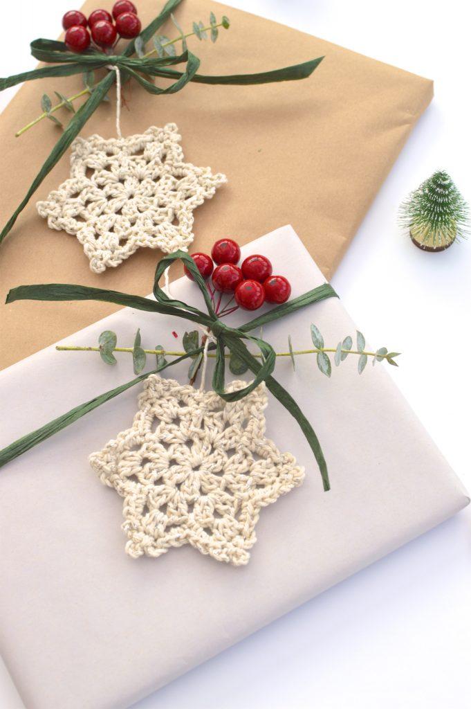 Christmas Snowflake made in cream yarn lay flat on a wrapped present with foliage and berries. 