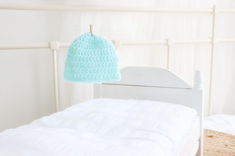 a turquoise baby beanie pegged up on fishing line in a white bedroom setting