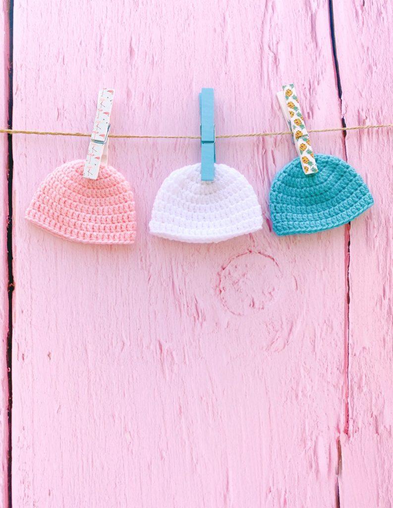 three abby beanie hats pegged up against a pink wooden fence 