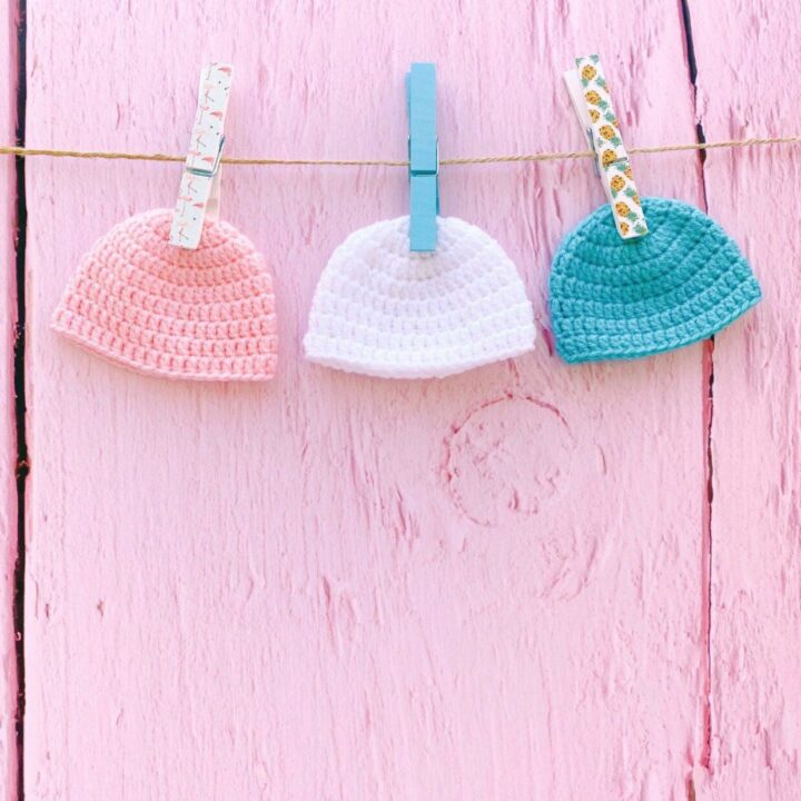 three abby beanie hats pegged up against a pink wooden fence