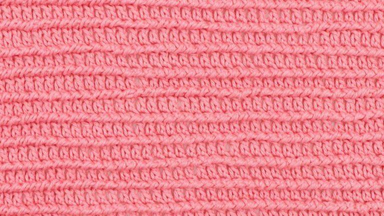 Close-up of a crocheted swatch using the corded ridge stitch in bright pink yarn, showing horizontal textured ridges and evenly spaced rows.