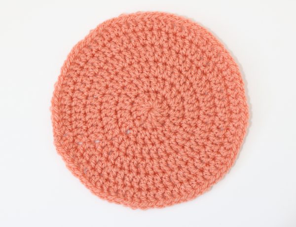 a flat lay image of a crochet flat circle made in orange yarn on a white background
