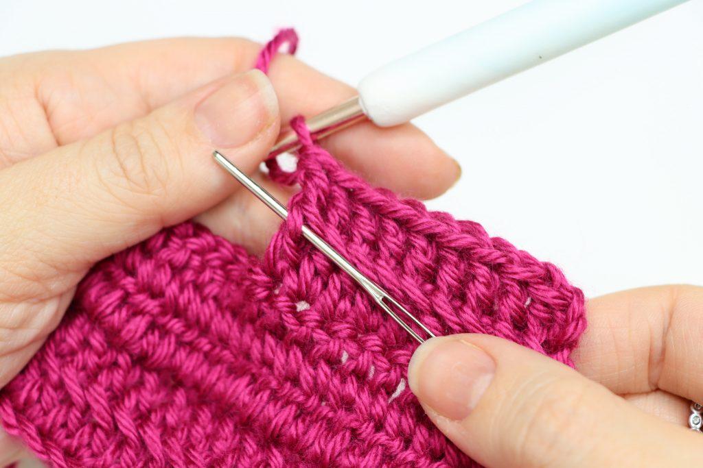 Fuchsia yarn and darning needle showing where to place stitch