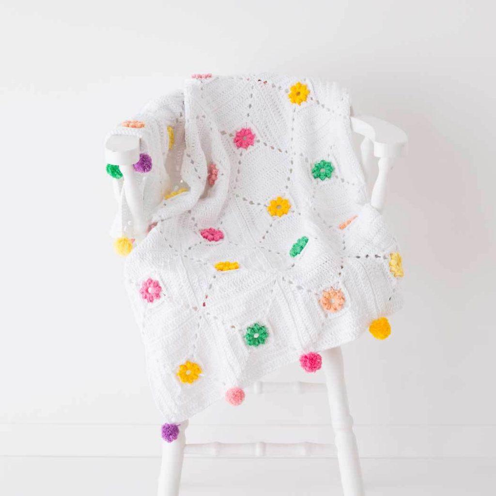 A white crochet blanket with bright flower accents