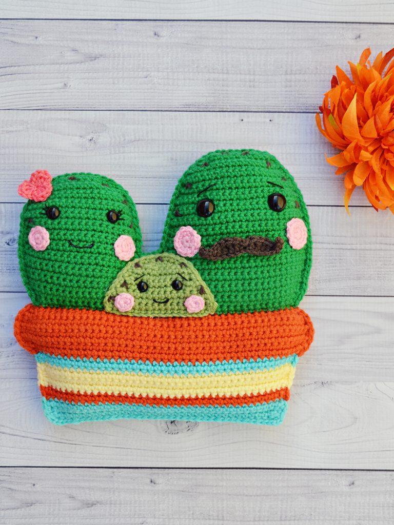 A trio of crochet cacti sit in a colourful crochet bowl. They are designed to look like a family, a father, a mother and a baby.