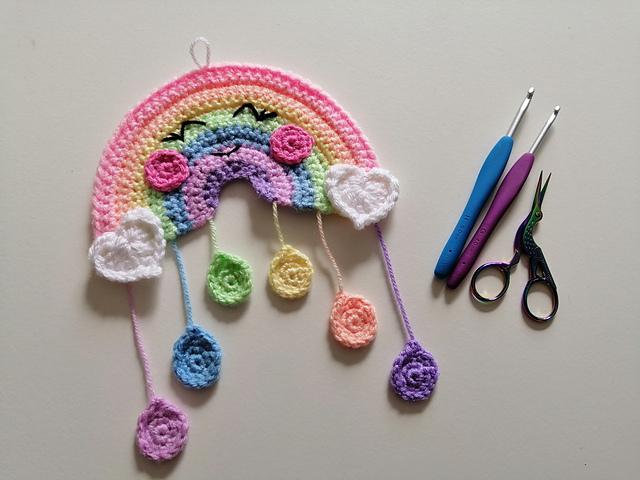 A small pastel rainbow made from crochet sits beside two hooks and some scissors