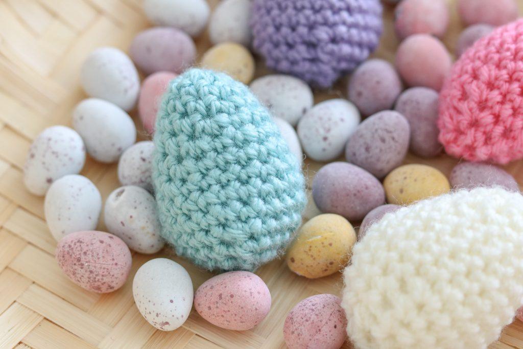 A quartet of pastel-coloured Easter eggs made from crochet sit beside chocolate mini eggs.