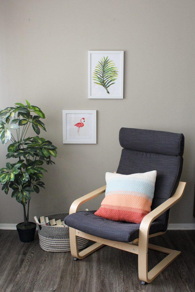 A Tunisian crochet pillow sits on a grey chair beside a  green plant