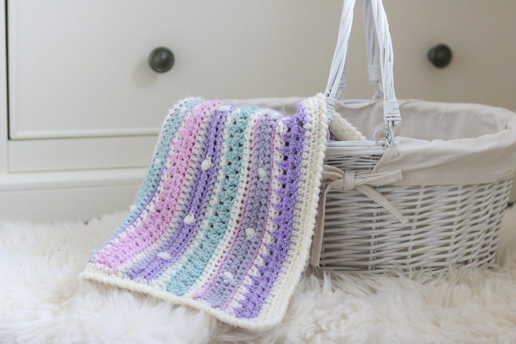 A pastel crochet blanket sit inside a white basket