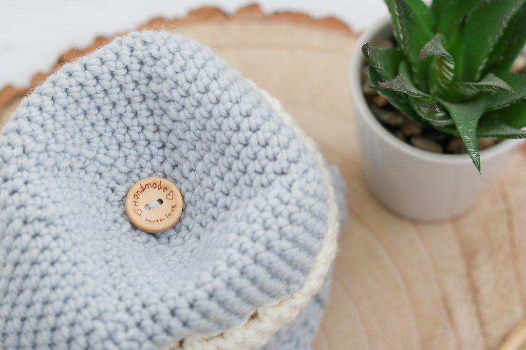 Close up of blue and white crochet hat with wooden button pom pom attachment