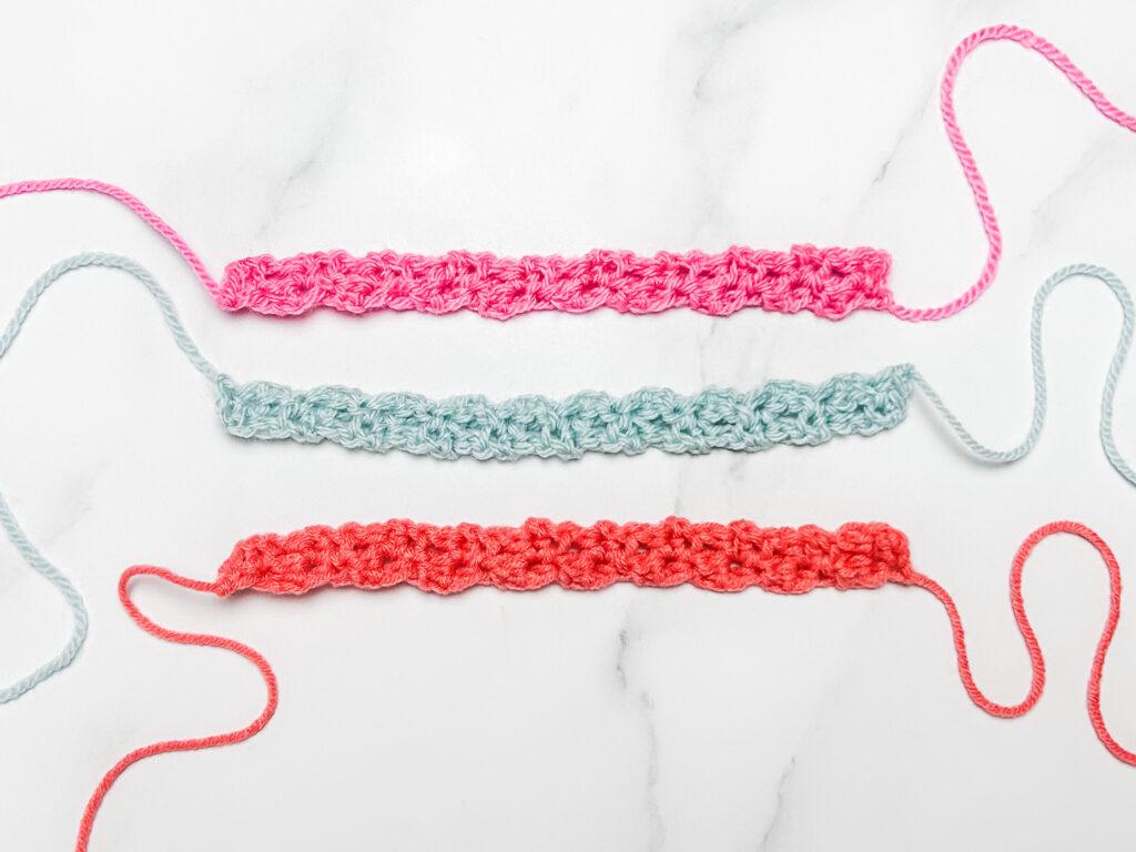 flay lay image of three crochet friendship bracelets in three colours, pink, pale blue and orange lay on a white marble backdrop. 