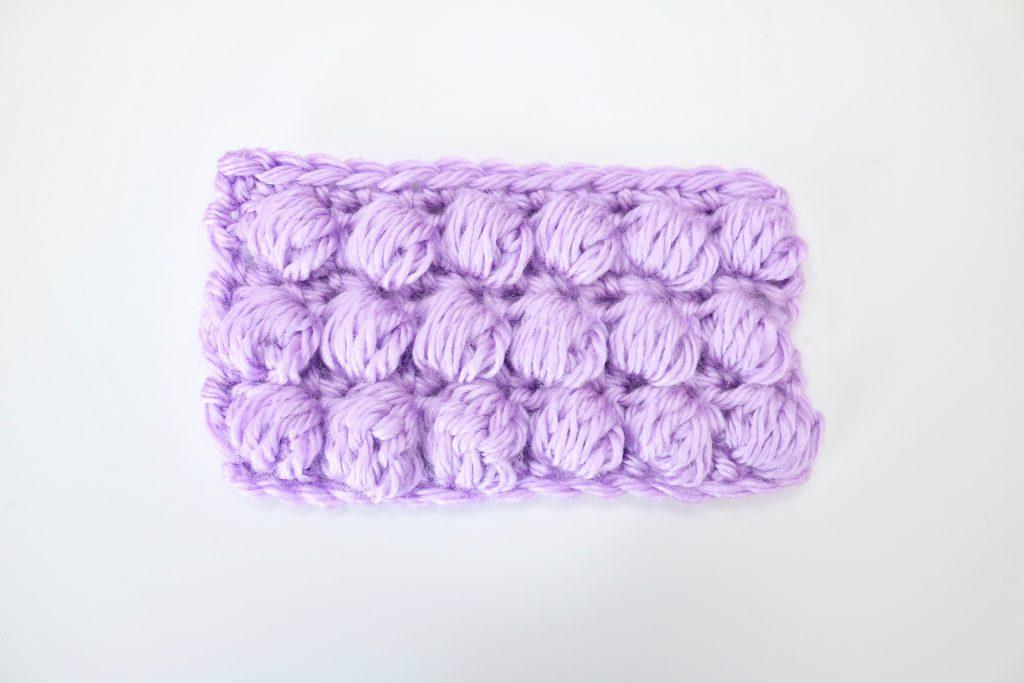A swatch of puff stitch in lilac yarn is shown against a white background. 