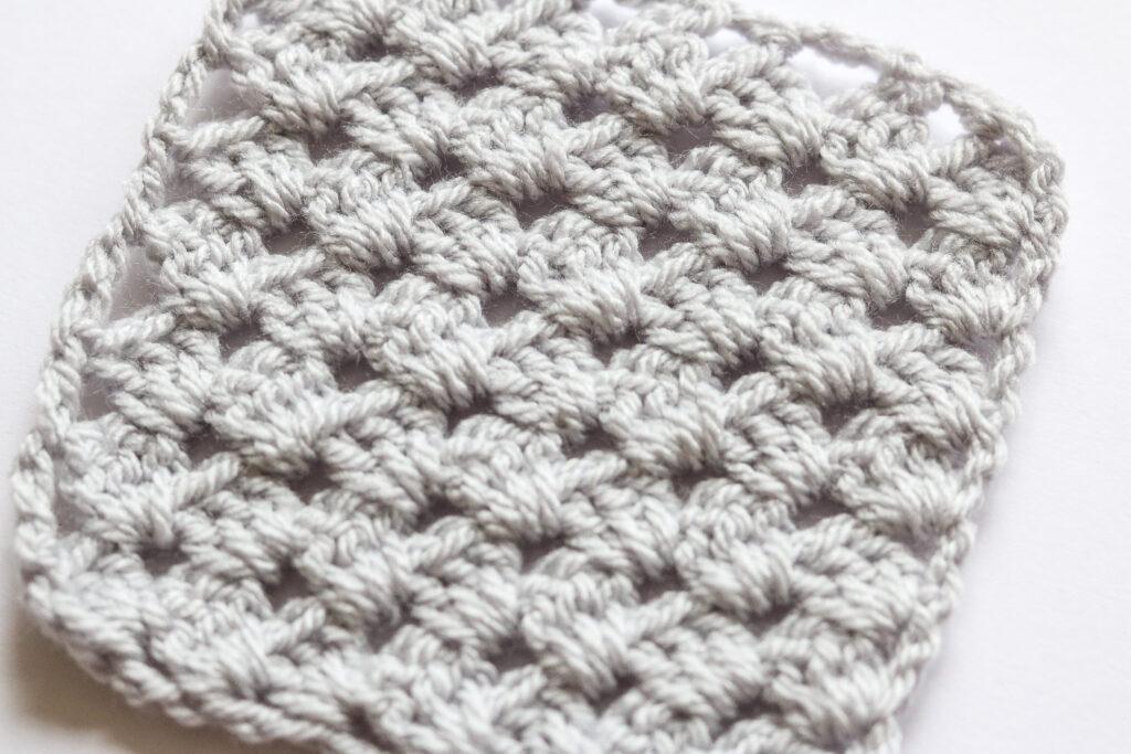 a grey c2c stitch granny square sits on a white background