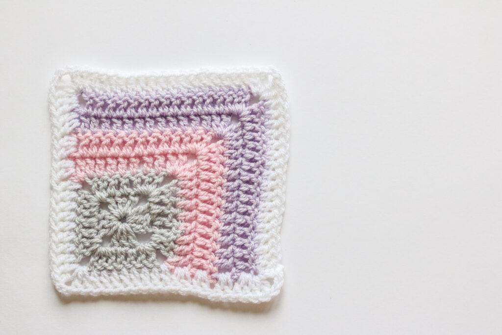 One mitered corner granny square in white, purple, pink and grey yarn.