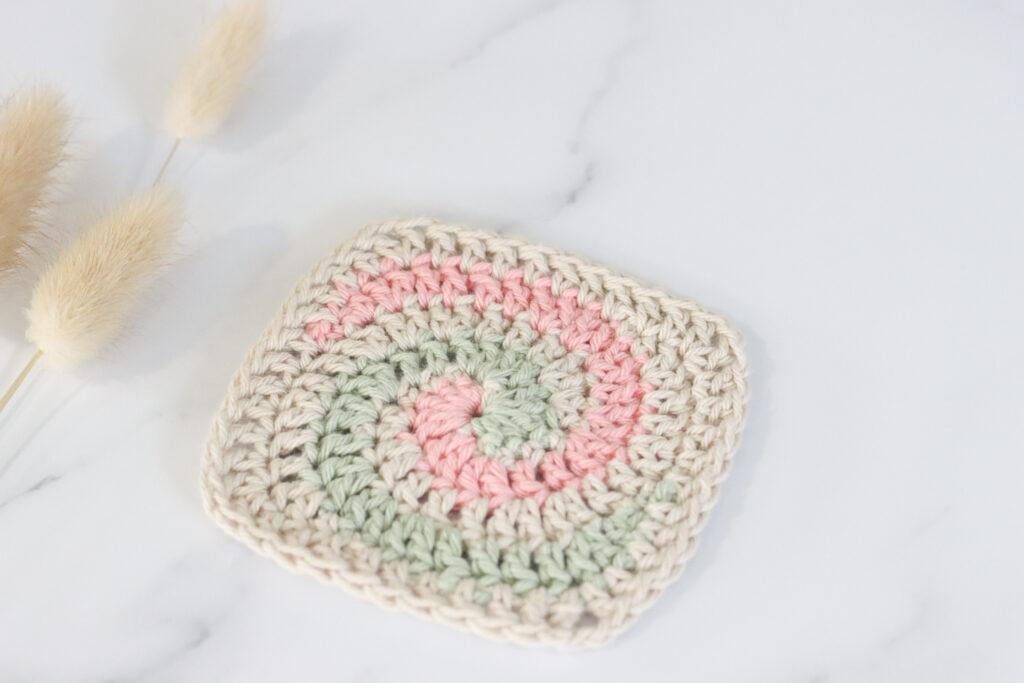 A spiral granny square on a marble background made from cream, green and pink yarn.