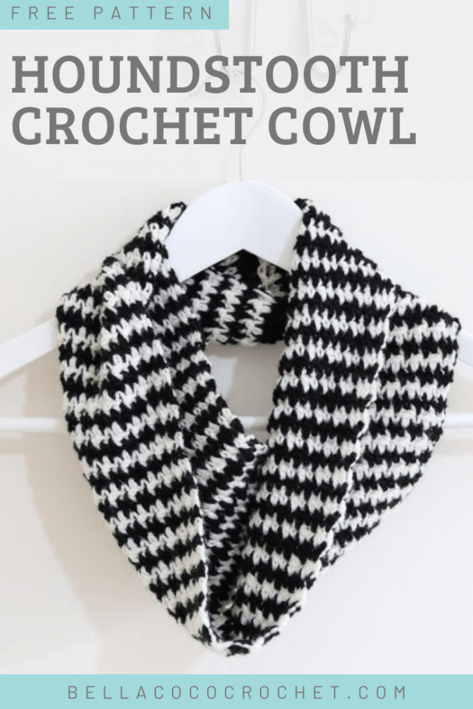 A crochet cowl in black and white is draped around a hanger. The stitches make up a houndstooth pattern.