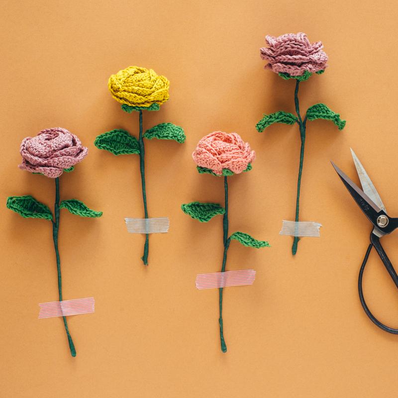 Several crocheted roses are taped to a warm orange background with washi tape. 