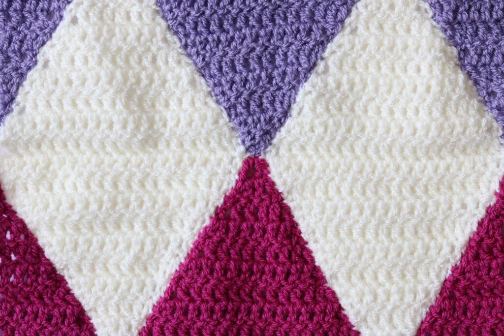 A crochet blanket with a diamond motif in shades of pink, white and purple.