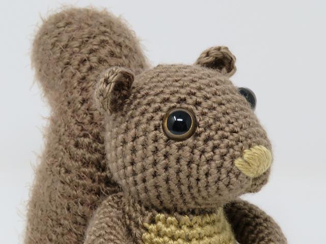 A crochet squirrel's face is show in close-up. He is made from a warm brown yarn.