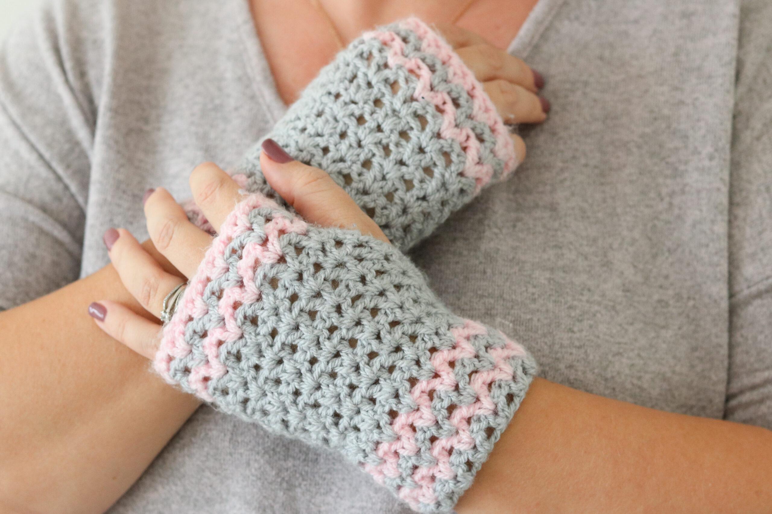 A woman wears a pair of grey and pink crochet wrist warmers. 