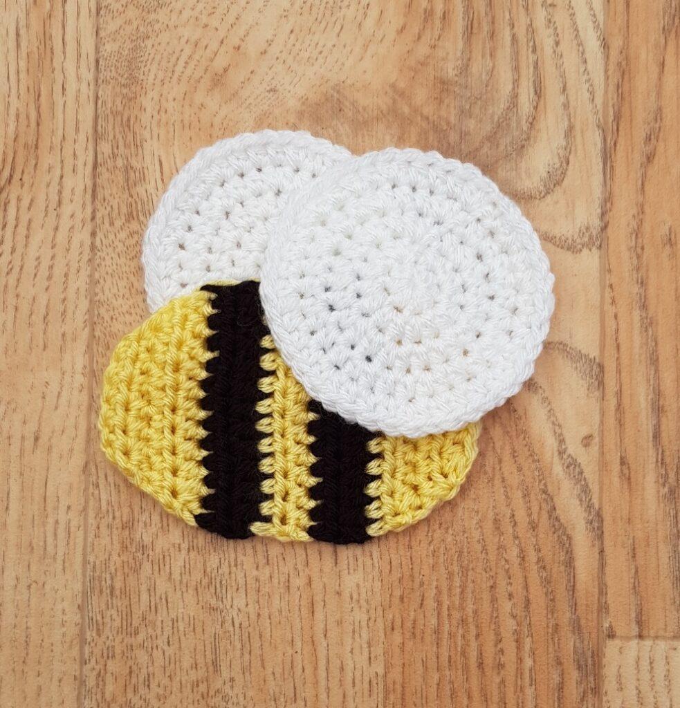 A crochet bee made from black, yellow and white yarn sits on a wooden background.