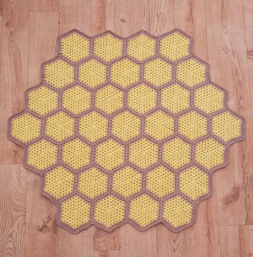 A bee crochet blanket in shades of yellow and brown sits on a wooden floor. There are yellow hexagons, but the bees are still to be added. 
