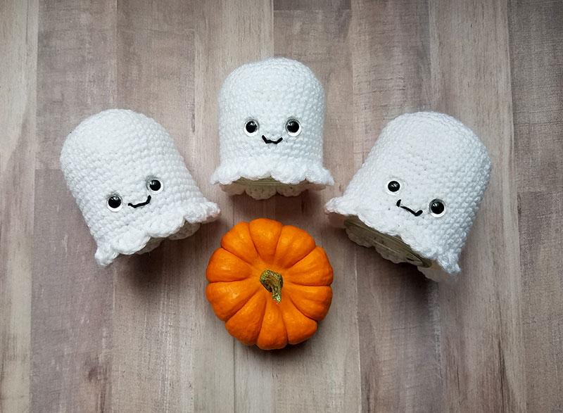 A trio of crochet ghosts in white yarn sit on a wooden background.