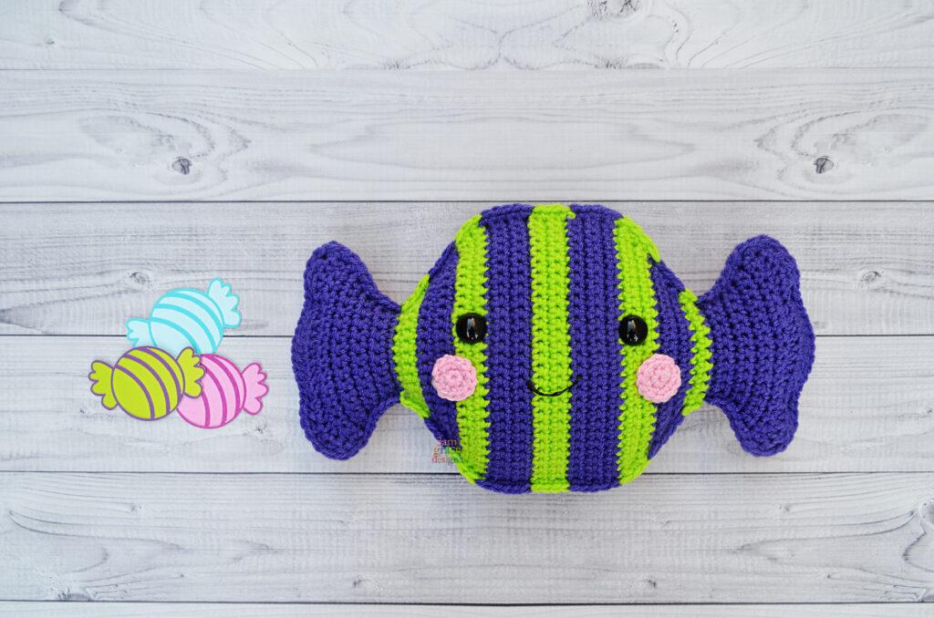 A crocheted candy in vibrant shades of purple and lime stripes sits on a wooden floor.