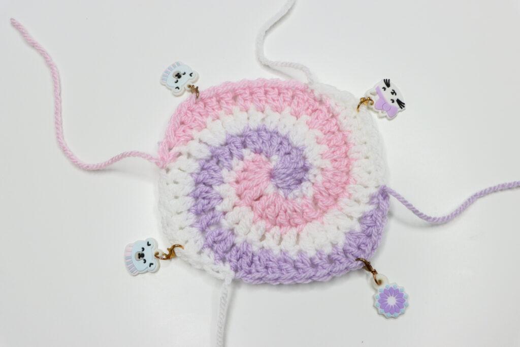A spiral granny square in pastel pink, purple, grey and white is in progress.