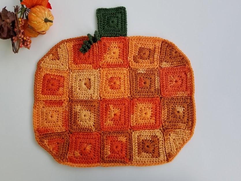 An orange coloured pumpkin made of crochet granny squares sits against a white backdrop.