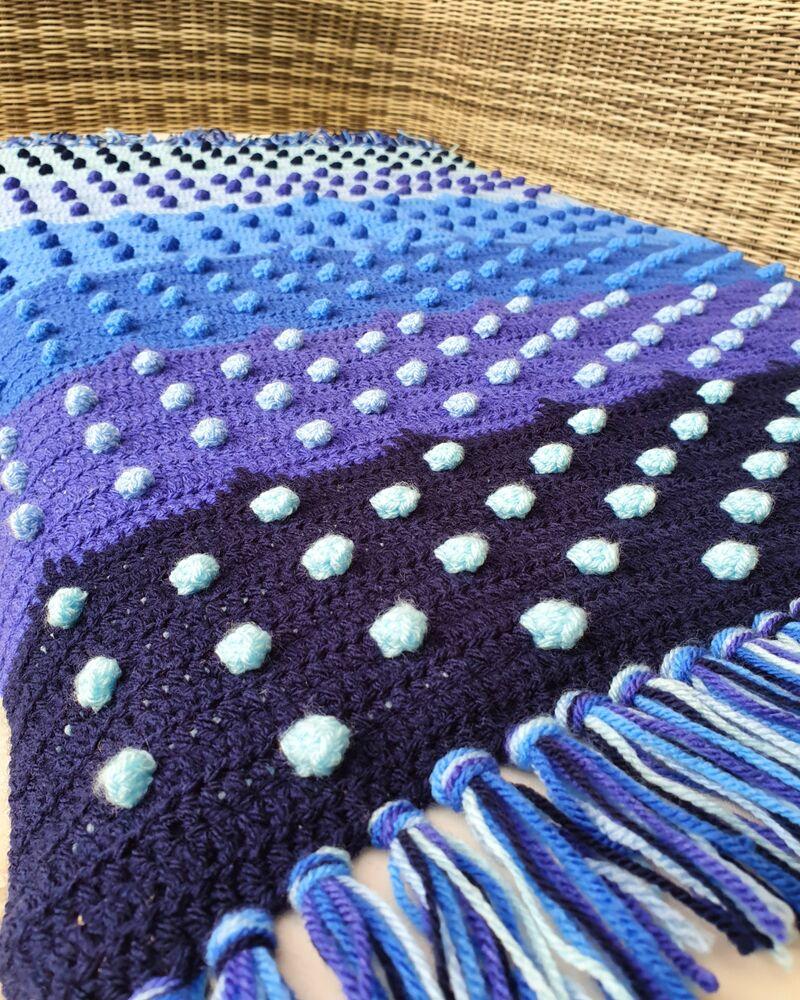 A blue ombre crochet blanket sits on a wicker chair. 