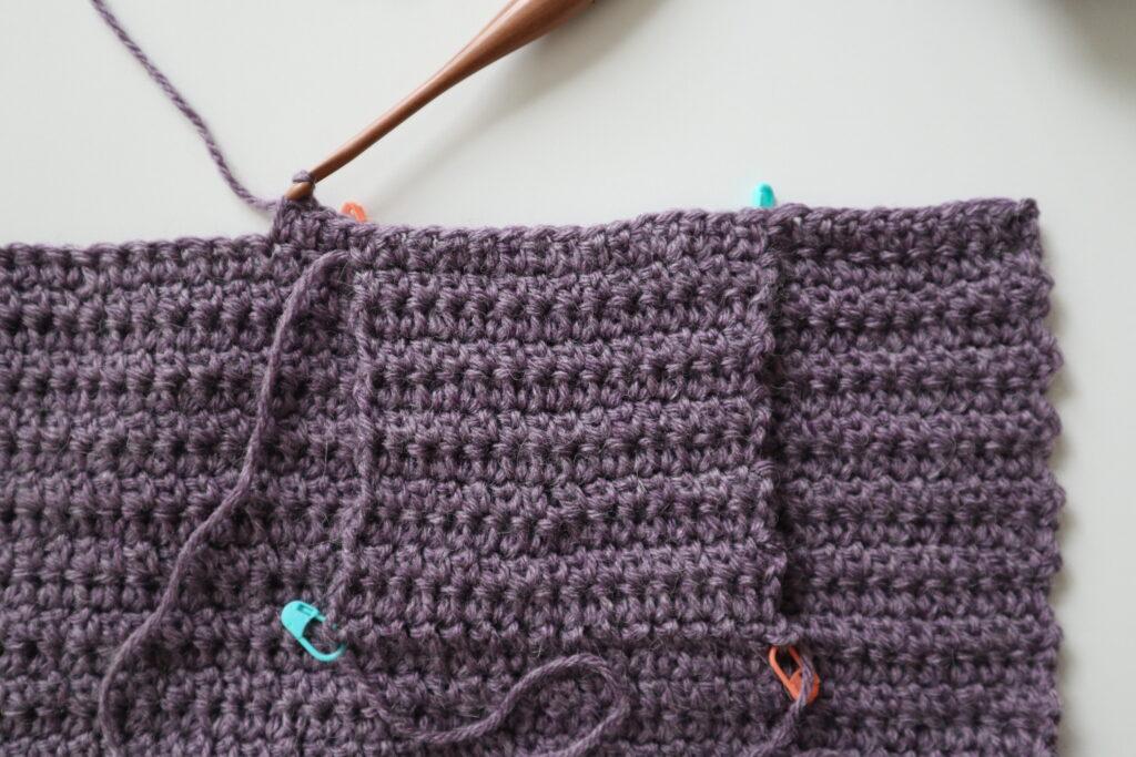 A swatch in purple yarn showing the construction of the crochet cardigan