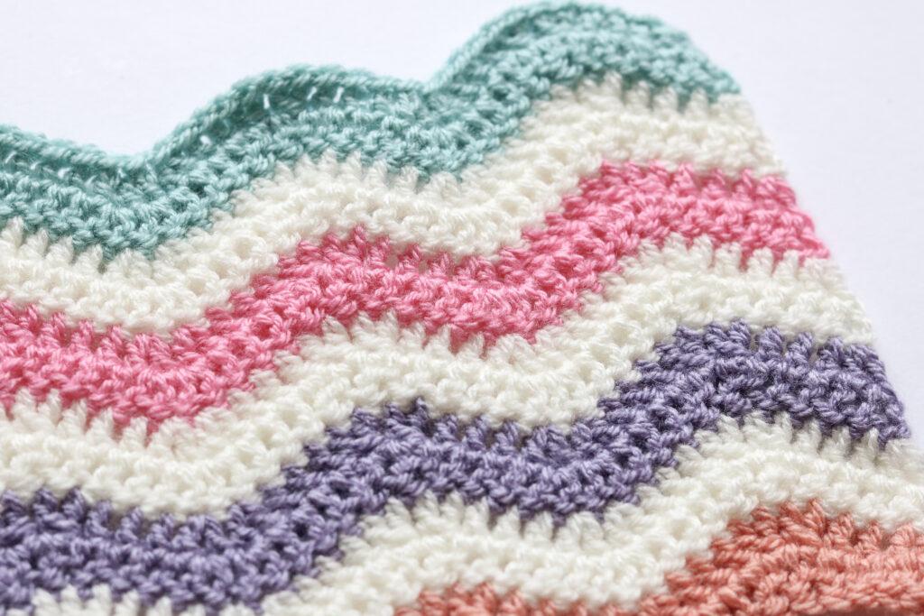 Crochet ripple stitch swatch in green, cream, pink, purple and peach yarn.