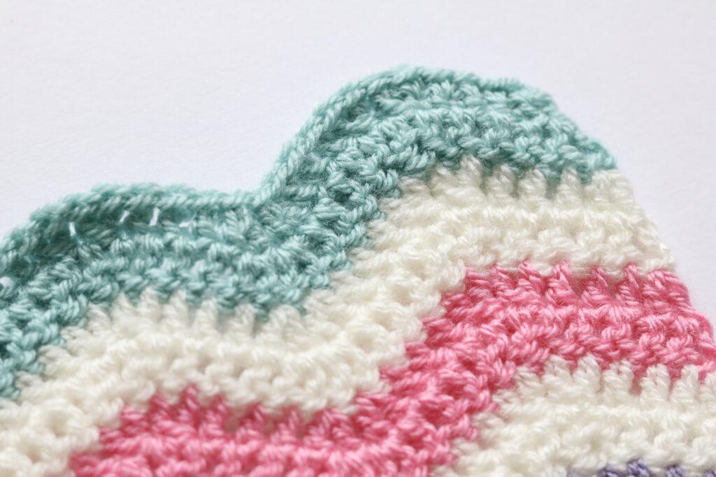 A close up of the crochet ripple stitch in green, cream, pink and purple yarn.
