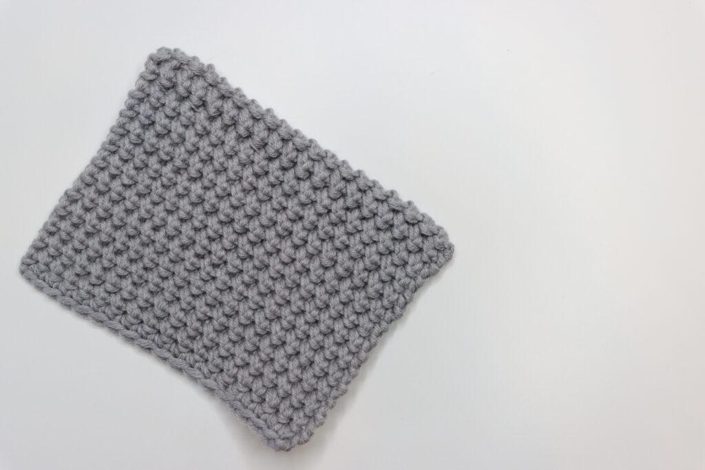A grey swatch of crocheted thermal stitch sits on a white background.