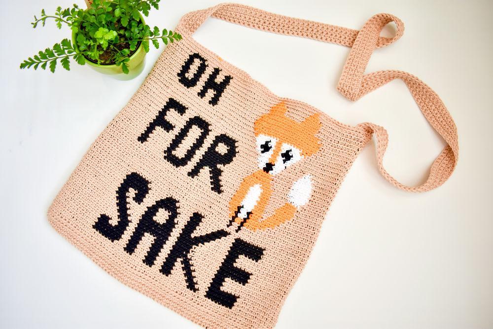 An oatmeal coloured tote bag with a crochet motif of a fox and the words "oh for sake" are arranged to read, "oh for fox sake".