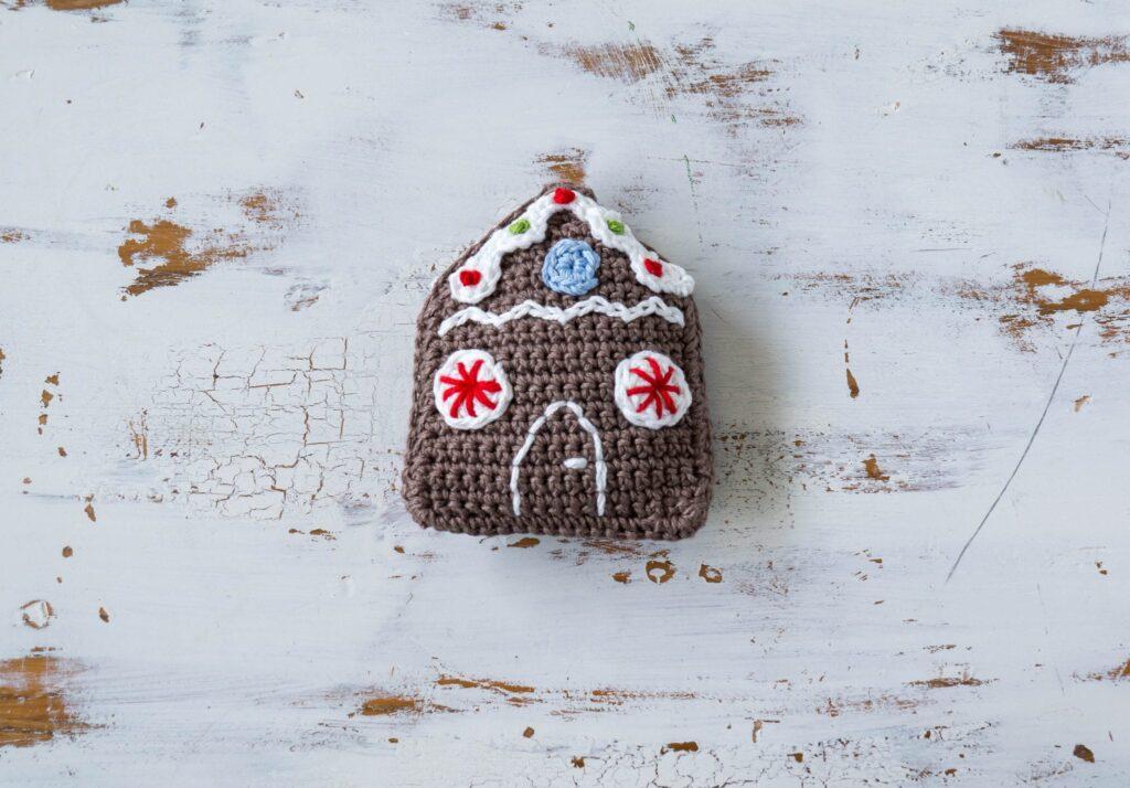 A small crochet gingerbread house sits on a white background. 